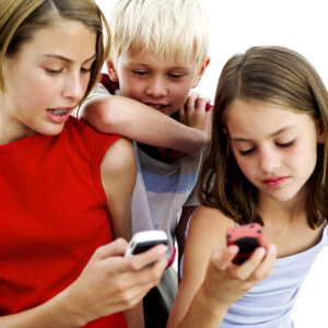 Young Girls Operating Cell Phones with a Young Boy (10-14) Standing Behind Them --- Image by © Royalty-Free/Corbis